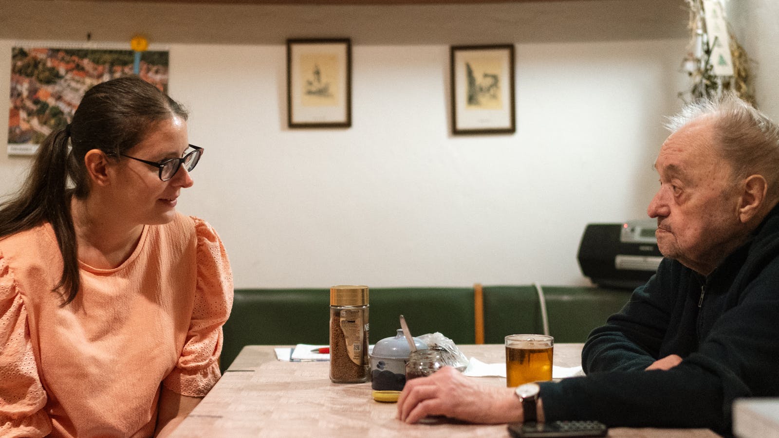An adult daughter and her father in conversation across a kitchen table over coffee