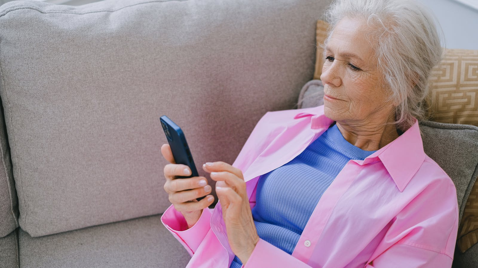An older woman on a sofa looking at her smartphone in a casual home moment